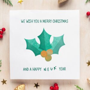 Square white christmas card on a neutral background with red and green confetti. The card says "We wish you a merry christmas and a happy neuk year", and has a stamped design of holly leaves and berries.
