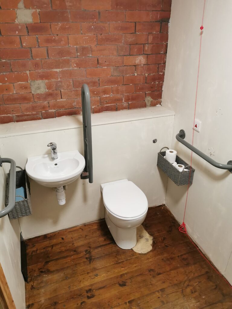 Photo of a disabled toilet with grab bars and a red emergency cord. However it is quite cramped.