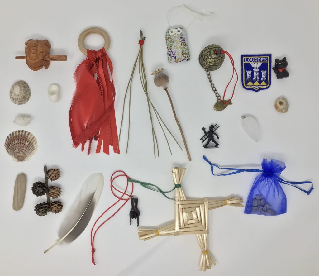 A selection of objects including shells, red ribbons on a wooden ring, dried plants, a blue organza bag, a straw St Brigid's Cross, and various amulets.