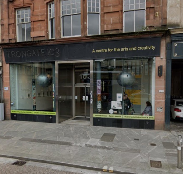 A building with a black and yellow frontage and large glass windows. There is a sign above the door that reads: "Trongate 103. A centre for the arts and creativity"