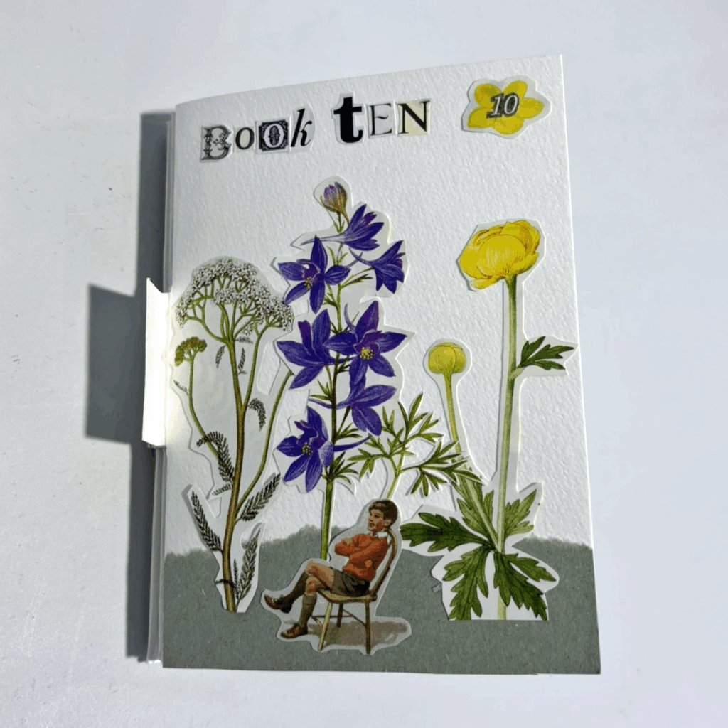 Small handmade booklet standing upright against a white background, with the cover titled “Book TEN” in mixed cut-out lettering. Botanical collage illustrations dominate the cover: tall stems of delicate white flowers, vivid purple bell-shaped blooms, and a bright yellow buttercup-like flower rise vertically across the page. Near the bottom, a small vintage-style cut-out figure of a seated child rests among the plants, creating the impression of being surrounded by oversized flowers. A yellow flower shape in the top right contains the number “10”. The overall design feels whimsical and collage-based, combining botanical imagery with found paper elements.