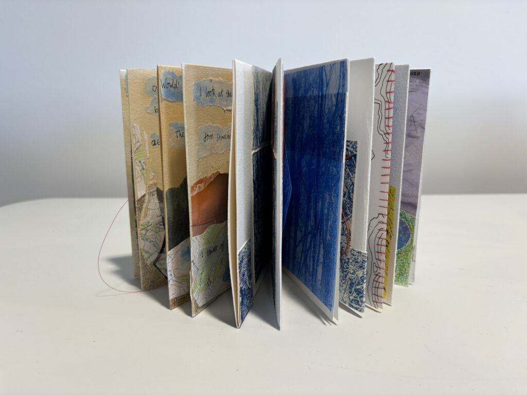 Small handmade accordion-style artist’s book displayed partially opened on a white surface against a plain grey background. Multiple folded pages fan out in a zigzag formation, revealing layered collaged elements including maps, torn paper, handwritten text fragments, blue-toned images, stitched red thread, and textured white card. The pages vary in colour and transparency, creating a sculptural, tactile sequence of images and materials. The overall effect is intricate and exploratory, inviting close looking and page-by-page discovery.