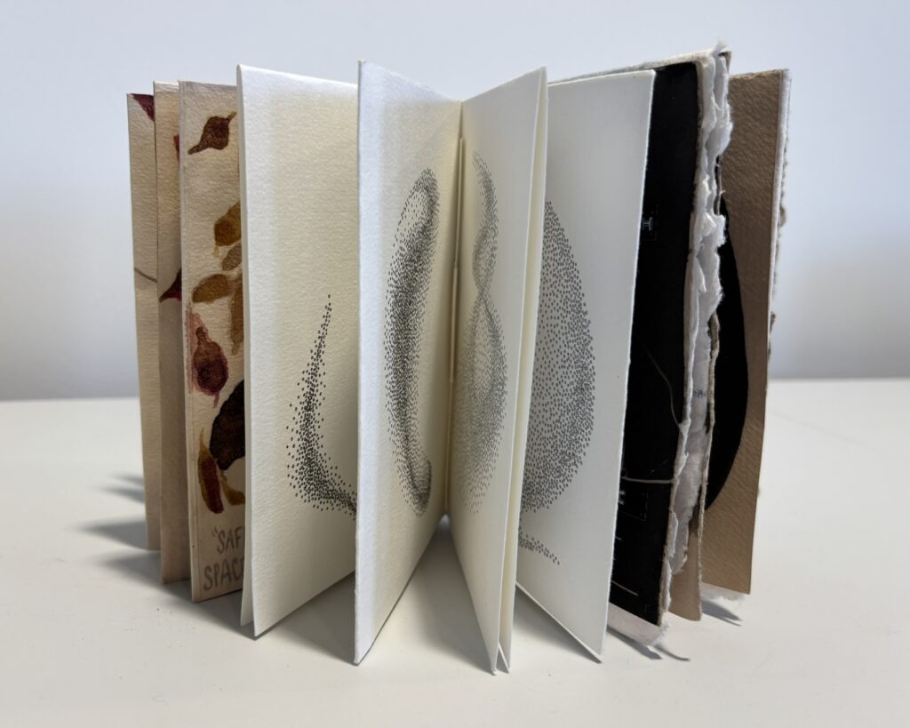the booklet standing open with its pages fanned out. Several inner pages display softly printed dotted forms in grey-black ink, each page revealing a slightly different abstract shape. The paper edges and cover boards are visible, emphasising the hand-bound, sculptural quality of the book.