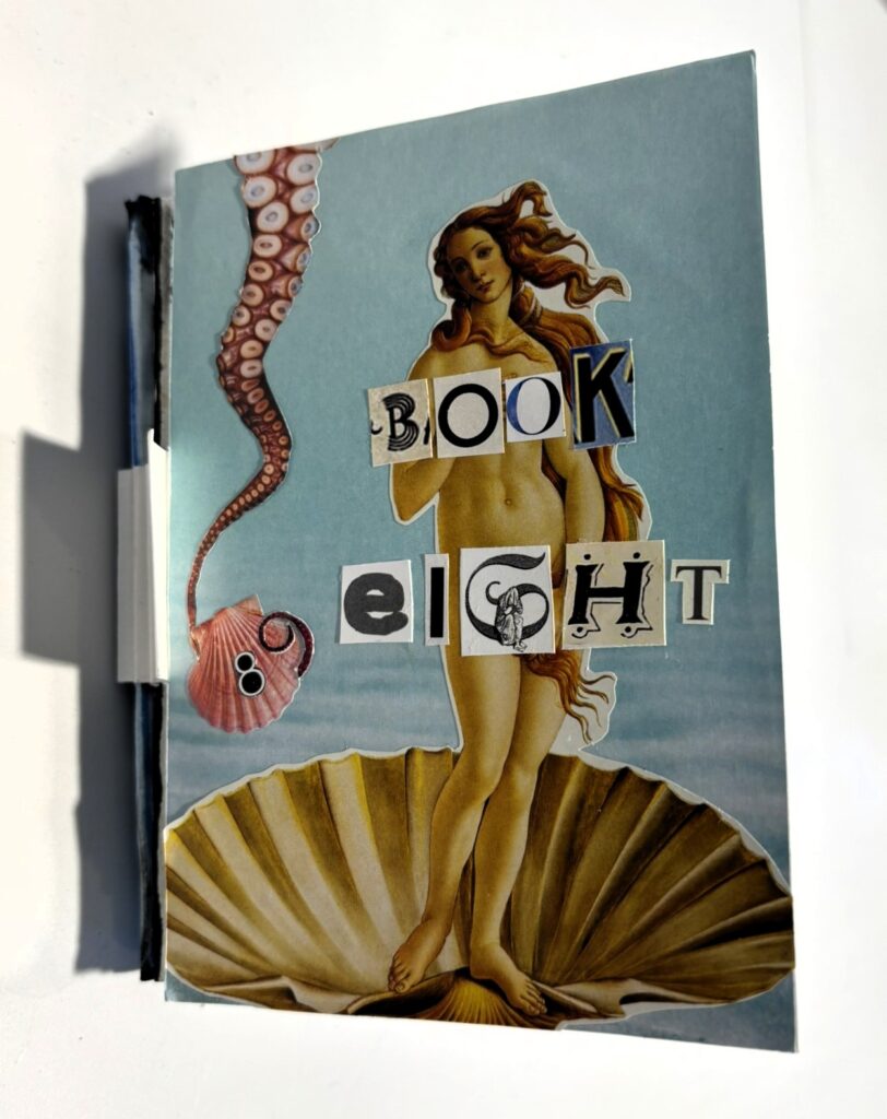 The cover of a handmade artist’s book shown upright against a white wall. The design is a collage on a pale blue background featuring a cut-out of Botticelli’s Birth of Venus: a nude female figure with long flowing auburn hair stands on a large scallop shell at the bottom of the cover. Across her torso, the title “BOOK EIGHT” is spelled out in mismatched ransom-note style cut-out letters from different typefaces and sizes. To the left, a pink scallop shell hangs from a curling octopus tentacle that descends from the top edge, its suckers clearly visible. A black spine is visible along the left side, emphasising the handmade, bound nature of the book. The overall effect is playful and surreal, blending classical art references with marine imagery and collage typography.