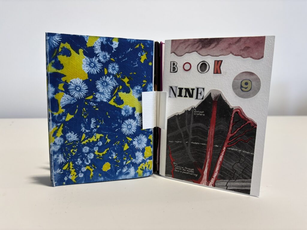 Small handmade artist’s book displayed open to show both the front cover and the final page. On the right, the front cover reads “BOOK NINE” in cut-out collage letters, with a circular “9” and a vintage cross-section illustration of a volcano with vivid red lava channels. On the left, the final page is a bold abstract composition in saturated cobalt blue with bright yellow patches and white floral or starburst-like printed forms scattered across the surface. A white folded tab or fastening strip sits between the two covers, emphasising the handmade construction. The contrast between the scientific volcano imagery and the vivid abstract back page gives the book a dynamic, visually layered presence.