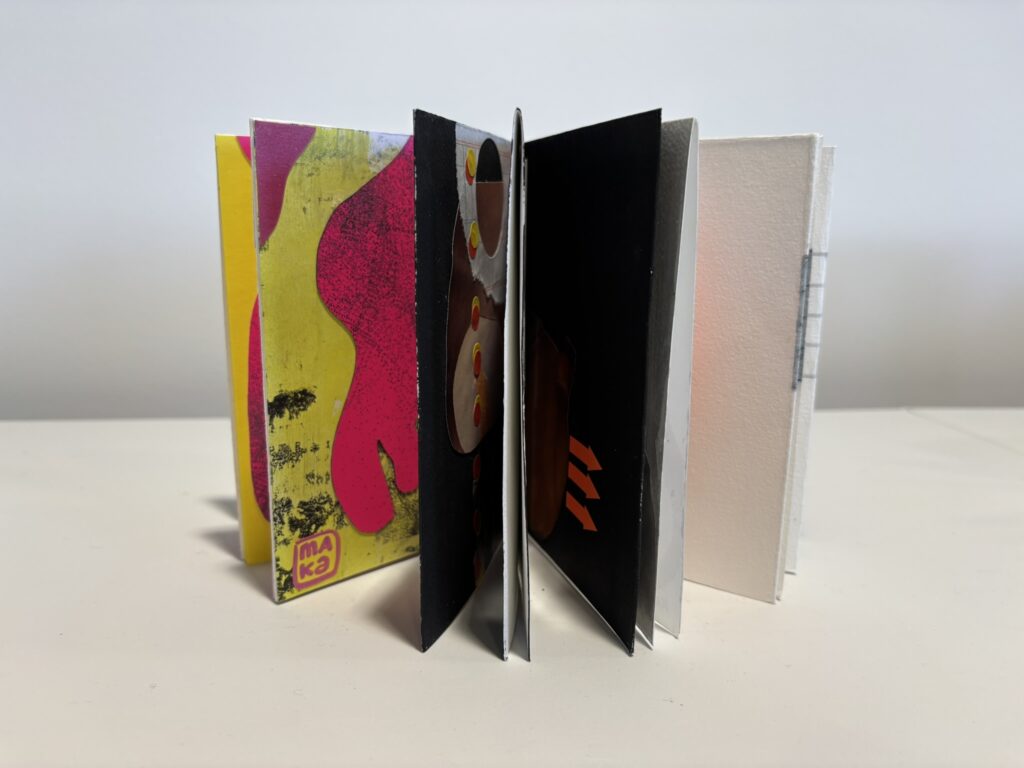 Artist’s book displayed upright with pages fanned open on a white surface. The visible pages form a sculptural, accordion-like arrangement with alternating black, white, and brightly coloured spreads. On the left, a vivid fluorescent yellow and hot pink cover or page features flowing abstract shapes and black textured marks. Deeper inside, glimpses of dark pages with circular cut-outs and orange geometric accents can be seen. The layered structure emphasises the book’s dimensional, handmade form.