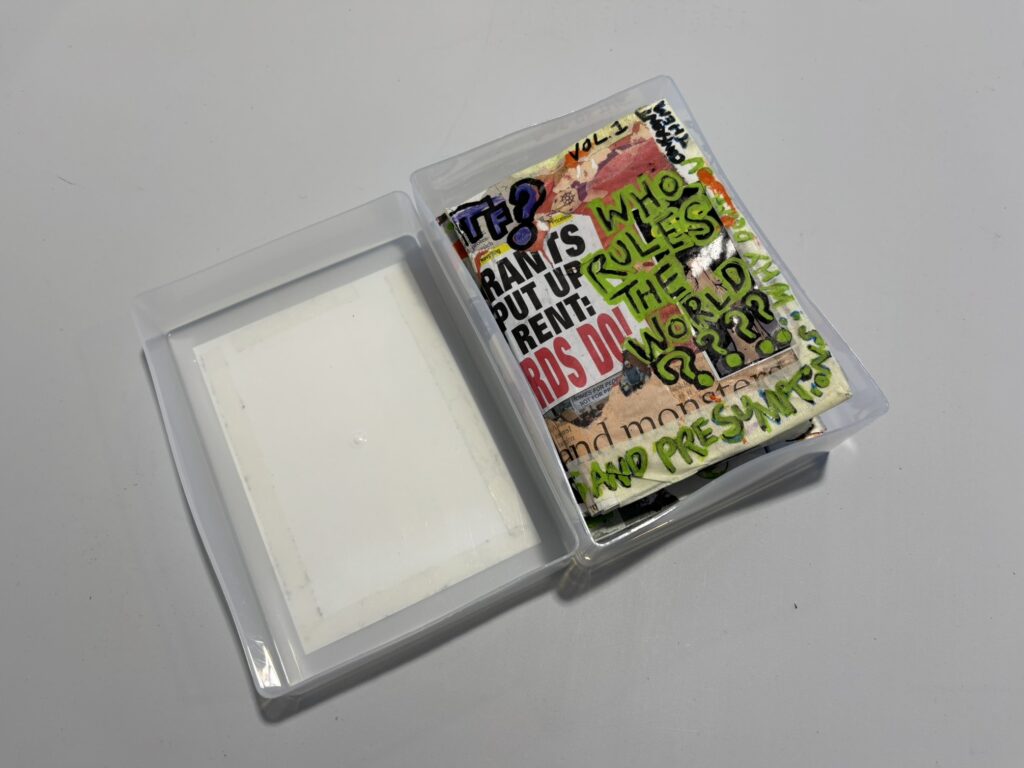 The same plastic box, open now, to reveal collaged books inside.
