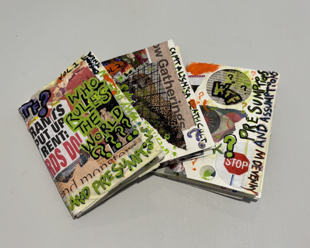 The three collaged books spread on a table. They are plastered in newspaper clippings, with handwritten annotations.